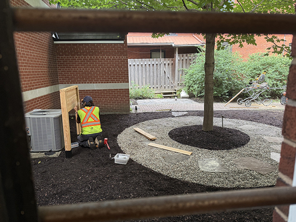 A worker in the garden area beside the tree outside the parish hall.
